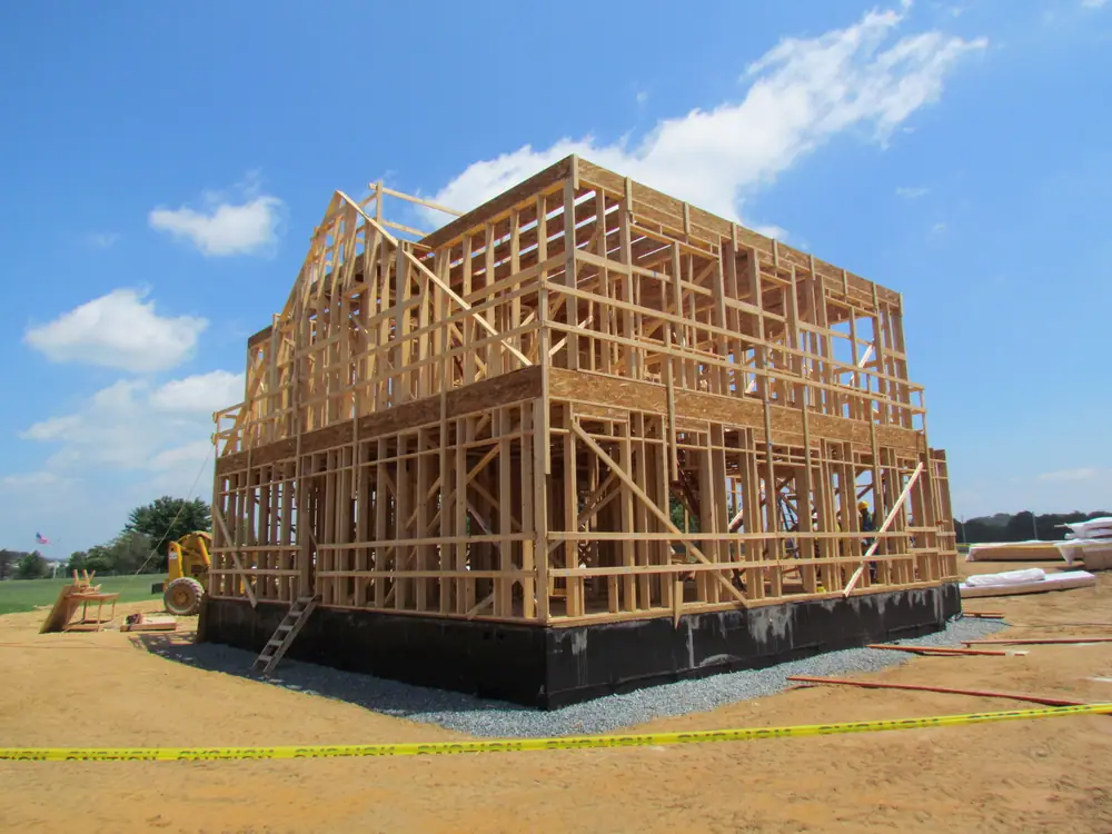 Two-story wooden frame of a house under construction on a dirt lot