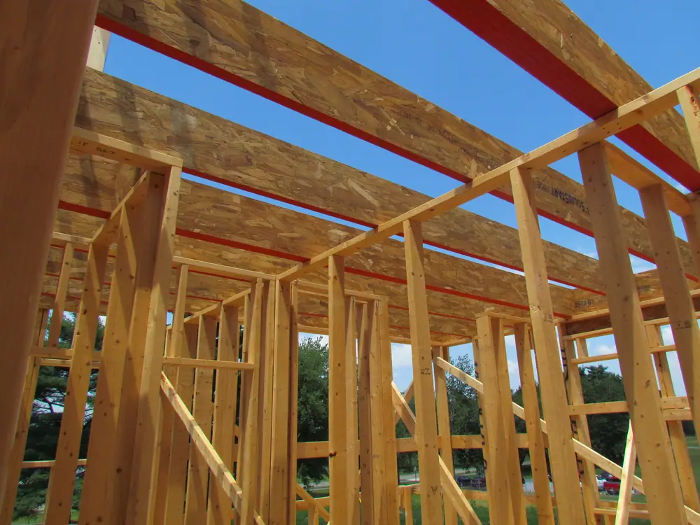 Wooden frame walls and ceiling beams of a house under construction against a blue sky